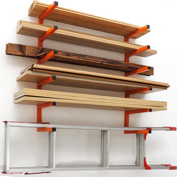 Orange six-level wall-mounted rack holding lumber and a ladder